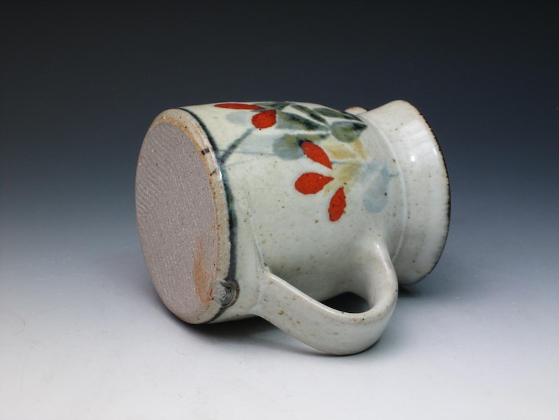 May include: A white ceramic mug with a handle, decorated with a floral design in red, green, and blue.