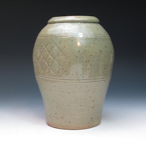 May include: A ceramic vase with a light grey glaze and a subtle speckled texture. The vase has a rounded body and a slightly flared lip. The surface is decorated with a raised geometric pattern.