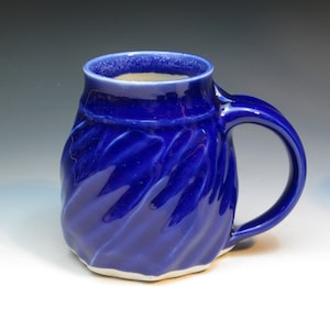 May include: A blue ceramic mug with a textured, wavy design. The mug has a white rim and a white base.