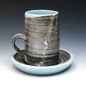 May include: A ceramic coffee cup and saucer set with a blue glaze and black and brown stripes. The cup has a handle and the saucer has a slightly raised edge.