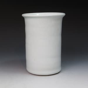 May include: A white ceramic vase with a cylindrical shape. The vase has a smooth, glossy finish.