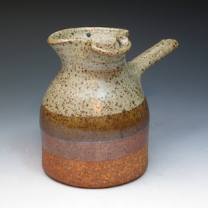 May include: A brown and white ceramic pitcher with a speckled glaze and a handle. The pitcher has three bands of brown, purple, and orange glaze.