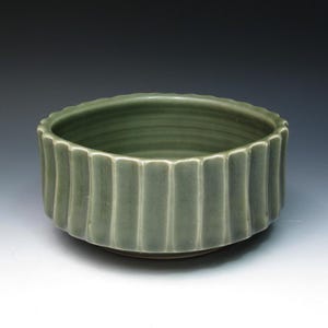 May include: A green ceramic bowl with a fluted design. The bowl is round and has a smooth, glossy finish.