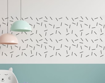 May include: A children's room with a white and teal color scheme, featuring a cat-shaped chair, a small table, and a wooden toy cart. The wall is decorated with black sprinkles. A white shelf displays toys and plants.