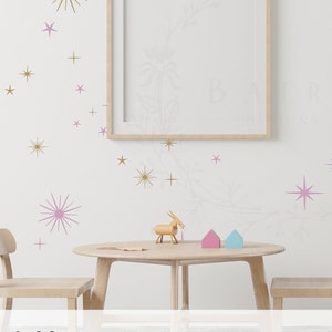 May include: A nursery room with a white wall decorated with gold and lilac star stickers. The room features a table and chairs, a toy car, and a toy bunny. The text "twinkle stars" and "Lilac / Gold" is visible at the bottom of the image.