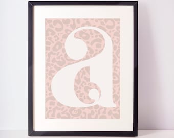 May include: A framed print with a white letter "A" on a pink leopard print background.