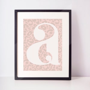 May include: A framed print featuring a white letter "A" on a pink leopard print background.