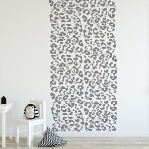 May include: A white wall with a vertical gray leopard print design. A white table, chair, and decorative items are in the foreground. A stuffed penguin sits on the chair. A framed cat illustration hangs on the wall.