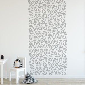 May include: A white wall with a vertical pattern of gray leopard print. A white table, chair, and decorative items are in the foreground. A stuffed penguin sits on the chair. A framed cat illustration hangs on the wall.