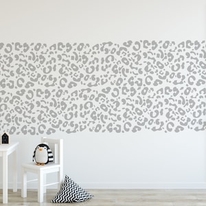 May include: A white wall with a gray leopard print pattern. A white table, chair, and decorative items are in front of the wall. A framed cat print and a stuffed penguin are also visible.