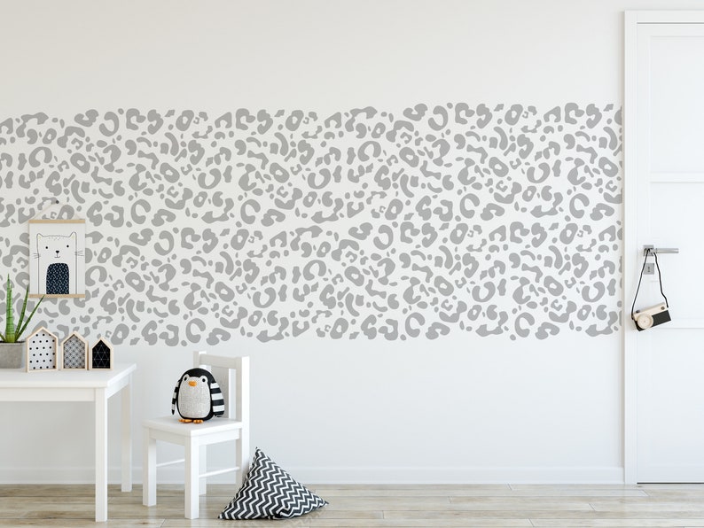 May include: A white wall with a gray leopard print pattern. A white table, chair, and decorative items are in front of the wall. A framed cat print and a stuffed penguin are also visible.