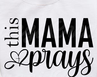 May include: White sweatshirt with the text "this MAMA prays" in black script. The sweatshirt is folded on top of blue jeans. A brown hat and a mug of coffee are in the background.