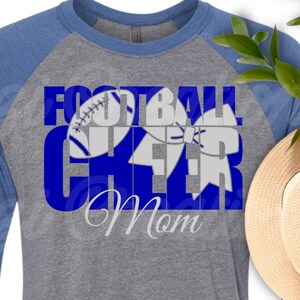 May include: A gray and blue long-sleeve shirt with the text "Football Cheer Mom" in blue letters. The text is layered with a white football and a white cheer bow.
