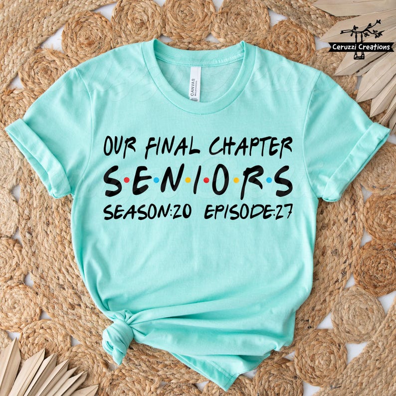 May include: A light teal t-shirt with the text "OUR FINAL CHAPTER SENIORS SEASON:20 EPISODE:27" in black, red, yellow, and blue. The shirt is knotted at the bottom and has rolled-up sleeves.