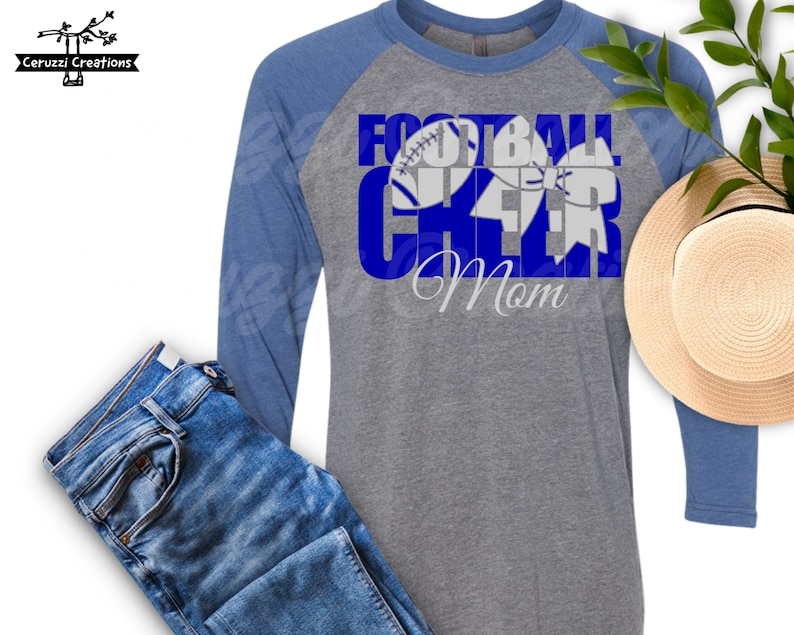 May include: A gray and blue long-sleeve shirt with the text "Football Cheer Mom" in blue letters. The text is layered with a white football and a white cheer bow.
