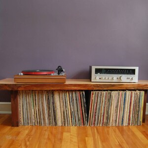 May include: A wooden record player stand with a turntable and amplifier on top. The stand has shelves filled with vinyl records.