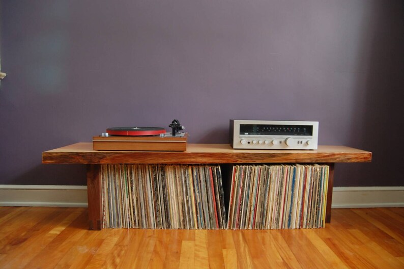 May include: A wooden record player stand with a turntable and amplifier on top. The stand has shelves filled with vinyl records.