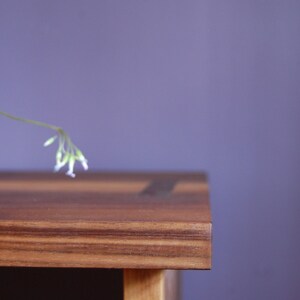 May include: A close-up of a wooden table top with a light brown finish. The table has a natural wood grain pattern and a smooth surface. The table is against a purple wall.