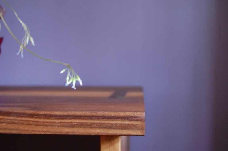 May include: A close-up of a wooden table top with a light brown finish. The table has a natural wood grain pattern and a smooth surface. The table is against a purple wall.