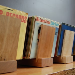May include: A set of five wooden record holders, each with a different colored vinyl record. The records have titles like "His Latest Flame" and "Little Sister".