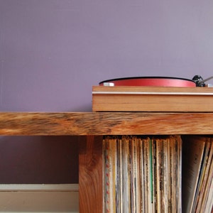 May include: A wooden record player stand with a turntable on top and shelves filled with vinyl records.