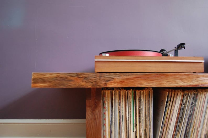 May include: A wooden record player stand with a turntable on top and shelves filled with vinyl records.