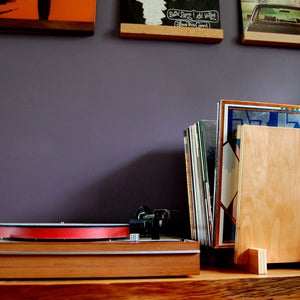 May include: A wooden record stand with a stack of vinyl records and a turntable on a wooden surface.