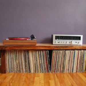 May include: A wooden record player stand with a turntable and amplifier on top. The stand has shelves filled with vinyl records.