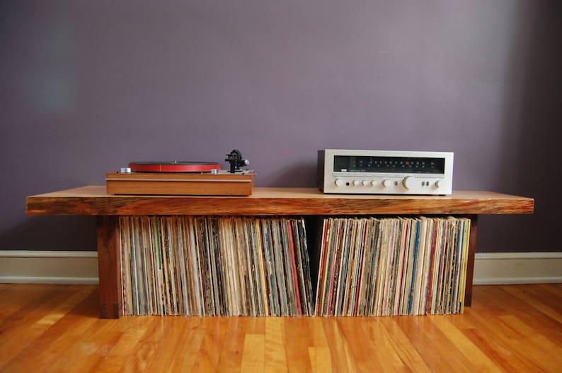 May include: A wooden record player stand with a turntable and amplifier on top. The stand has shelves filled with vinyl records.