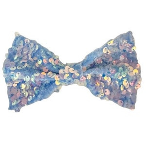 Puede incluir: Un lazo azul claro con lentejuelas iridiscentes. El lazo está hecho de terciopelo y tiene una textura suave y delicada.