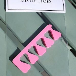 May include: A pink foam toe separator with a heart-shaped design, packaged in a clear plastic sleeve. The top of the package has a label that reads "For your MISTLE...TOES".
