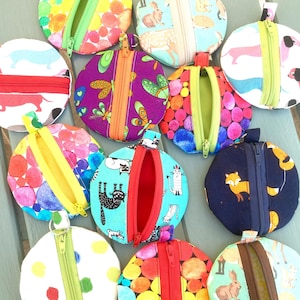 May include: A collection of ten round zippered pouches with various colourful patterns. The pouches are made of fabric and have a zipper closure. The patterns include polka dots, animals, and abstract designs.