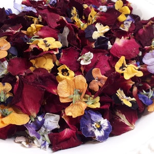 May include: A close-up of a white bowl filled with dried flower petals. The petals are a mix of deep red, yellow, orange, purple, and blue. The arrangement is dense and colorful, showcasing the natural beauty of the dried flowers.