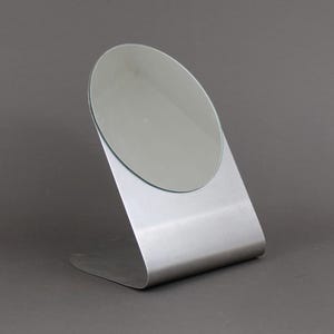 May include: A silver-coloured tabletop mirror with a round, slightly angled mirror surface.