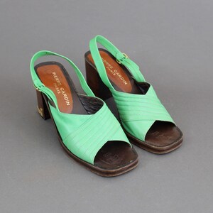 May include: A pair of green leather heeled sandals with a buckle closure. The sandals are labeled "Pierre Cardin Paris".