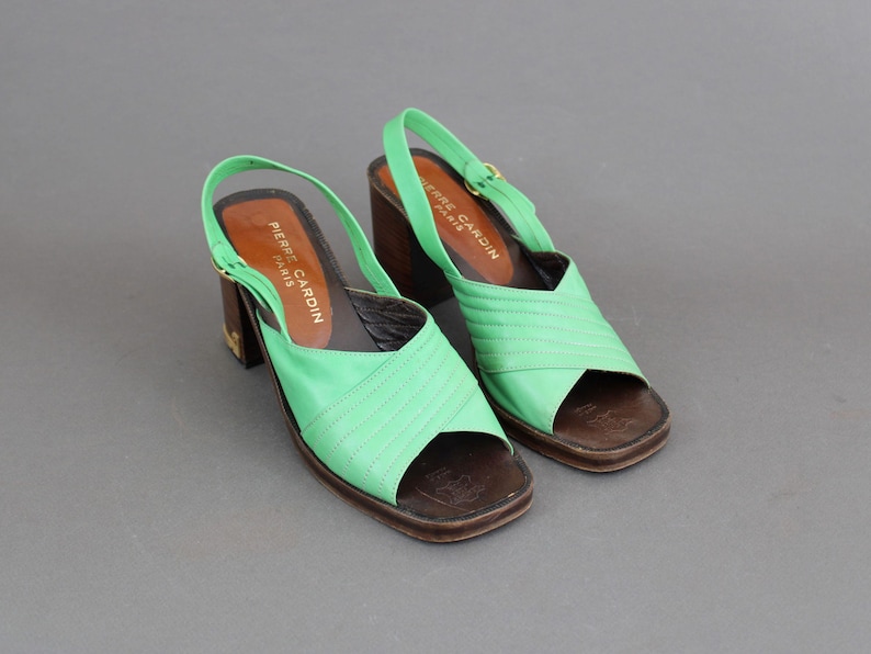 May include: A pair of green leather heeled sandals with a buckle closure. The sandals are labeled "Pierre Cardin Paris".