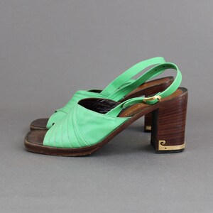 May include: A pair of green leather heeled sandals with a wooden platform and a gold buckle. The sandals have a criss-cross strap design.