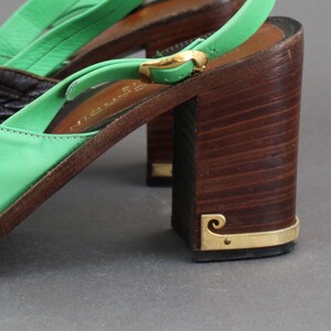 May include: Green leather heeled sandals with a wooden platform and a gold buckle. The sandals have a slingback strap and a closed toe.
