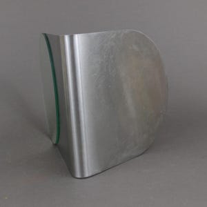 May include: A silver metal bookend with a curved shape and a clear glass panel on the side.