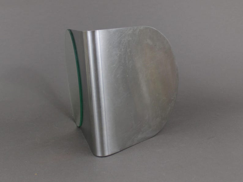 May include: A silver metal bookend with a curved shape and a clear glass panel on the side.