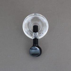 May include: A black screw with a clear plastic cap. The screw has a round, black knob at the end.