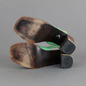 May include: A pair of green platform sandals with a gold buckle. The sandals have a wooden sole and a thick heel.