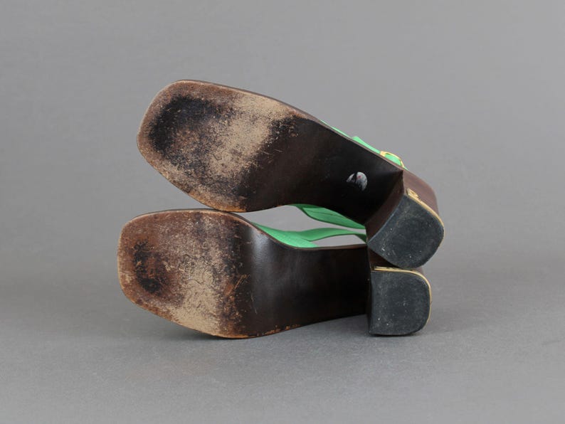 May include: A pair of green platform sandals with a gold buckle. The sandals have a wooden sole and a thick heel.