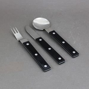 May include: A set of three silver utensils with black handles and white dots. The set includes a fork, a knife, and a spoon.