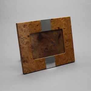 May include: A square wooden picture frame with a natural burl wood finish. A vertical silver metal stripe accents the frame. The frame has a rectangular opening for a photograph.