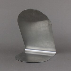May include: A silver metal bookend with a curved design. The bookend is made from a single piece of metal and has a smooth, polished finish.
