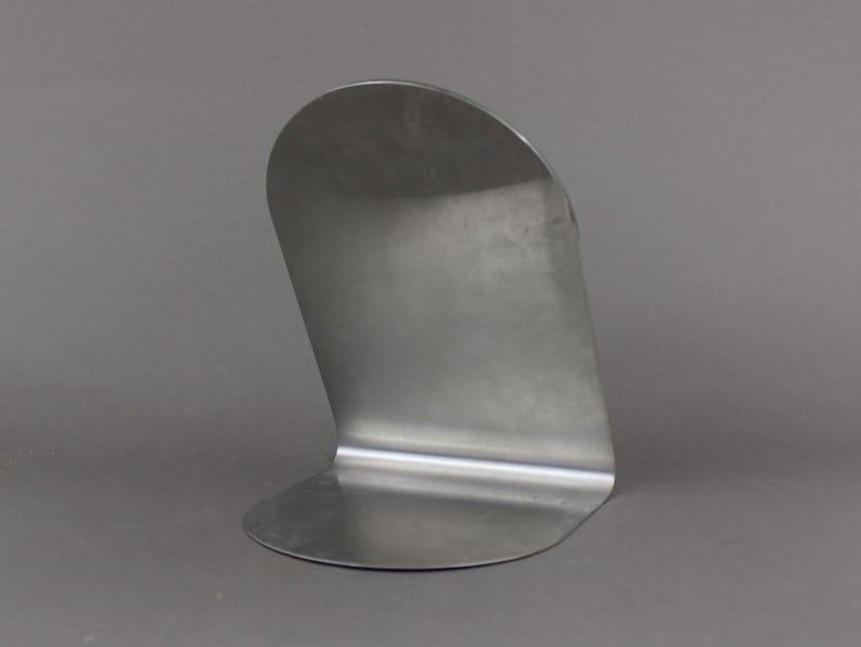 May include: A silver metal bookend with a curved design. The bookend is made from a single piece of metal and has a smooth, polished finish.