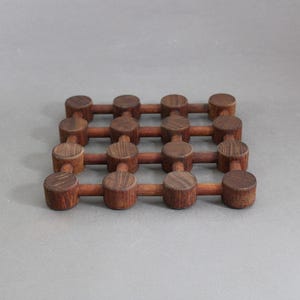 May include: A wooden trivet with a grid design. The trivet is made of dark brown wood and features cylindrical pieces connected by bars. The design is simple and functional, suitable for kitchen use. The trivet is approximately 20 cm x 20 cm.