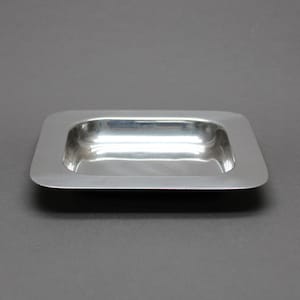 Peut inclure: Un plateau rectangulaire en acier inoxydable avec une finition polie et réfléchissante et des coins arrondis. Le plateau présente un bassin central peu profond et encastré entouré d'un large bord plat et lisse, au design métallique épuré.