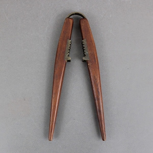 May include: A wooden nutcracker with a brass hinge and teeth. The nutcracker is brown and has a long, pointed handle.